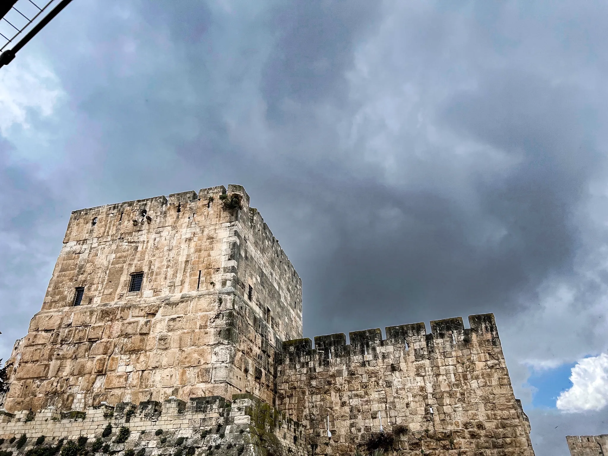 A stone tower and rampart of Jerusalem's Old City under heavy cloud