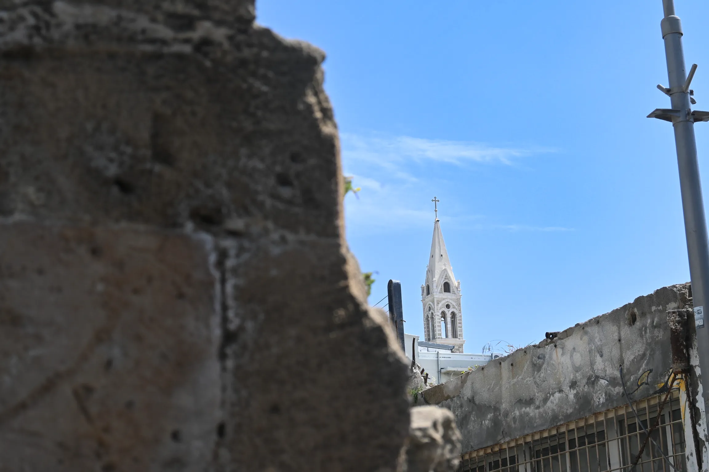A church spire rising behind a broken stone wall under a clear sky