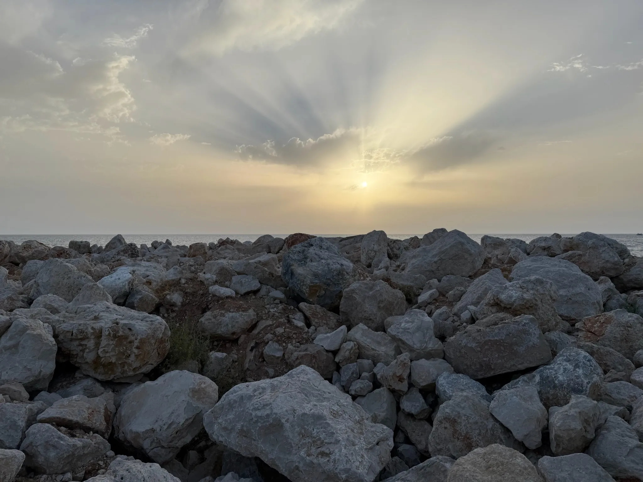 Sun breaking through cloud over a rocky shoreline at dawn